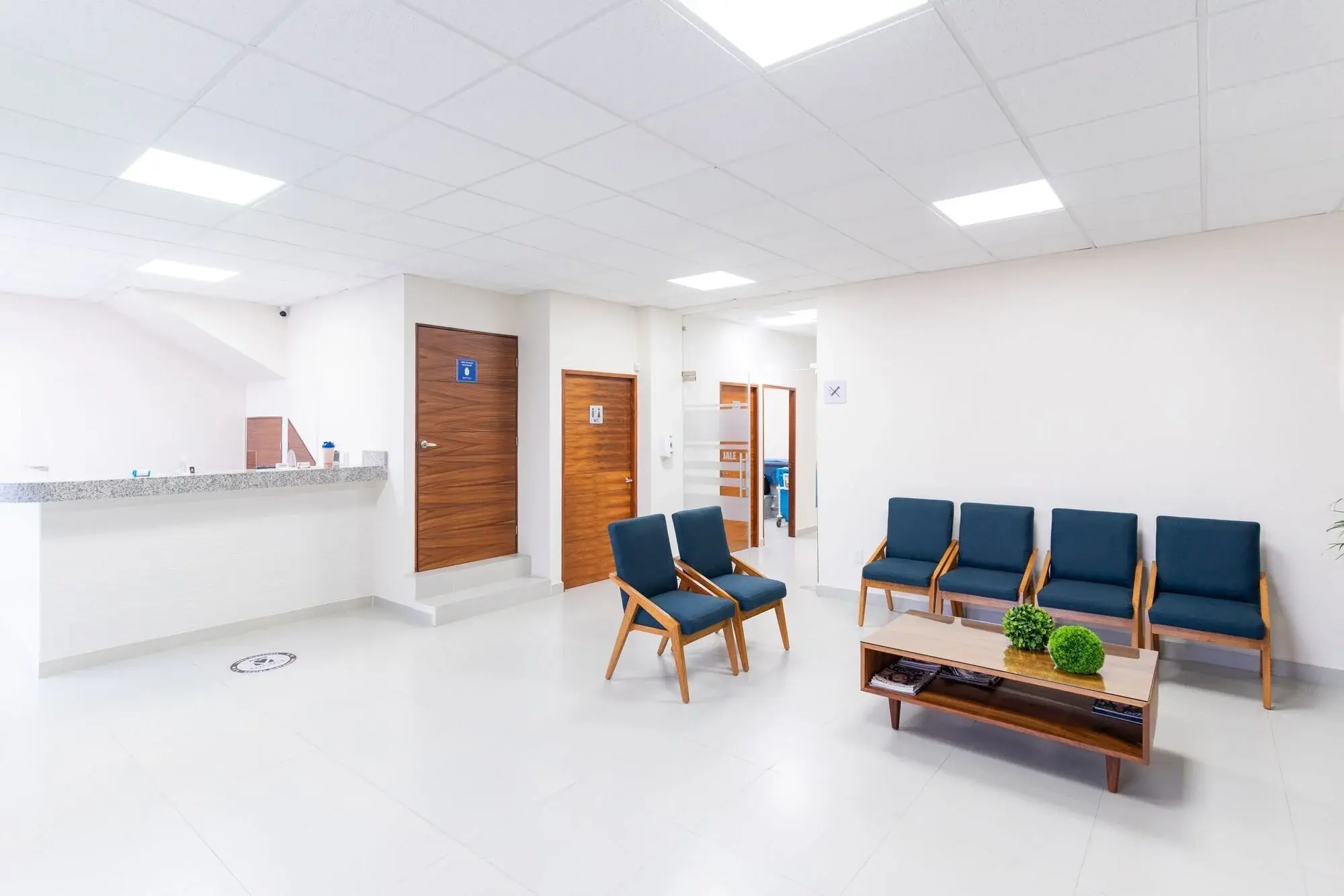 Salle d’attente claire avec fauteuils bleus et table basse.